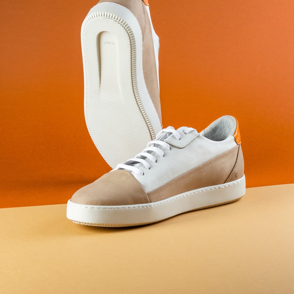 white and light brown sneakers standing against an orange background